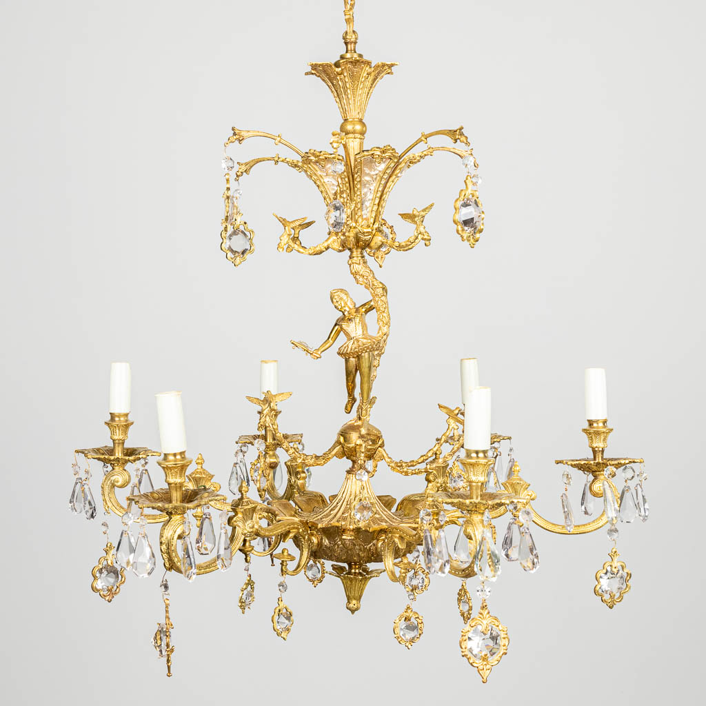 A chandelier made of brass and glass, decorated with birds and a ballet dancer