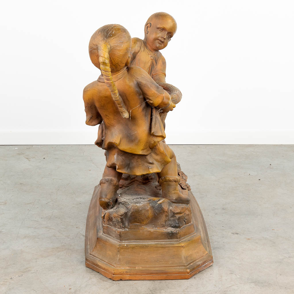 Een groot terracotta beeld van twee kinderen met een mand, gemerkt 