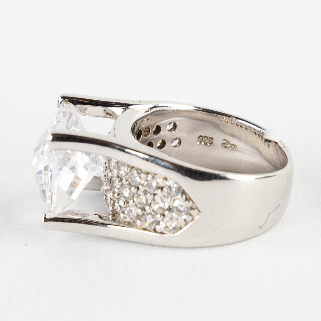 Een ring met grote vierkante gefacetteerde steen/glas, en kleinere stenen. Zilver, gemerkt 925.