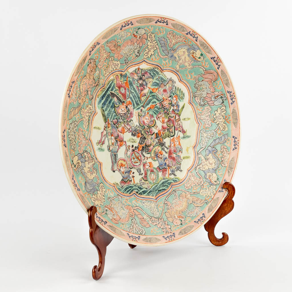 A Chinese Famille Rose plate, decorated with warriors, peaches and Foo Dogs. 19th/20th C. (D:45,5 cm)