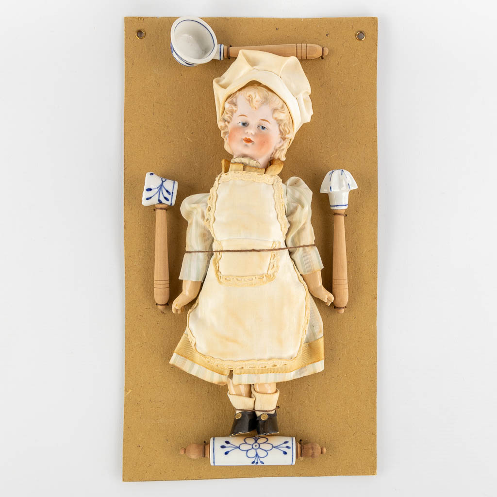 William Goebel, 'Boy Chef' a porcelain doll mounted on a cardboard with accessories. (W:20,5 x H:37 cm)