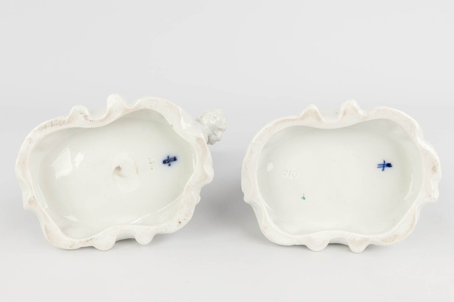 Sitzendorf, A pair of porcelain flower vases in the shape of 2 putti holding a shoe. (L: 12,5 x W: 16 x H: 25 cm)
