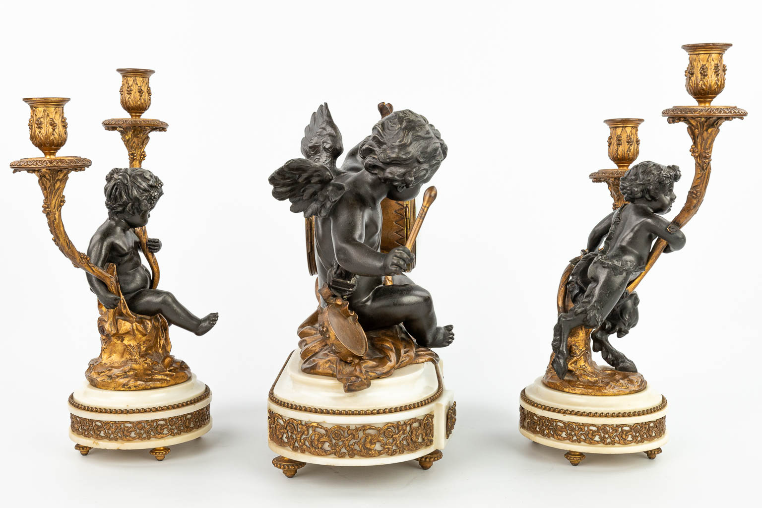 A three-piece mantle clock decorated with putti and a satyr, made of patinated and gilt spelter. (H:37cm)
