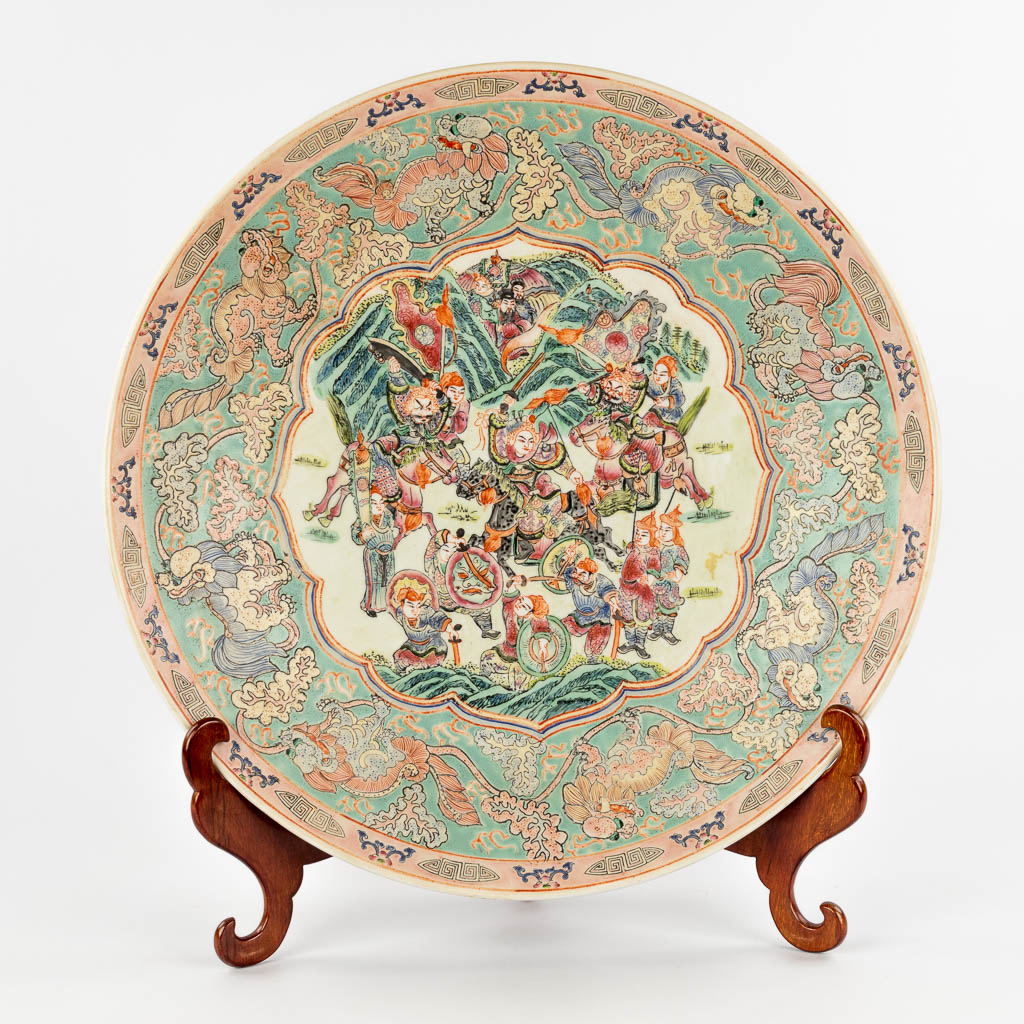 A Chinese Famille Rose plate, decorated with warriors, peaches and Foo Dogs. 19th/20th C. (D:45,5 cm)