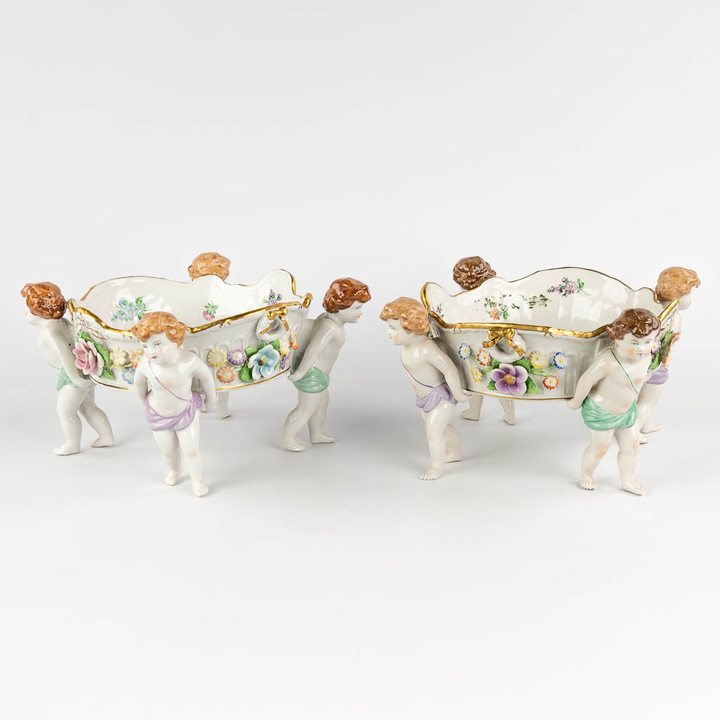 Two baskets, carried by putti. Polychrome German porcelain, 20th C. (H:17 x D:33 cm)