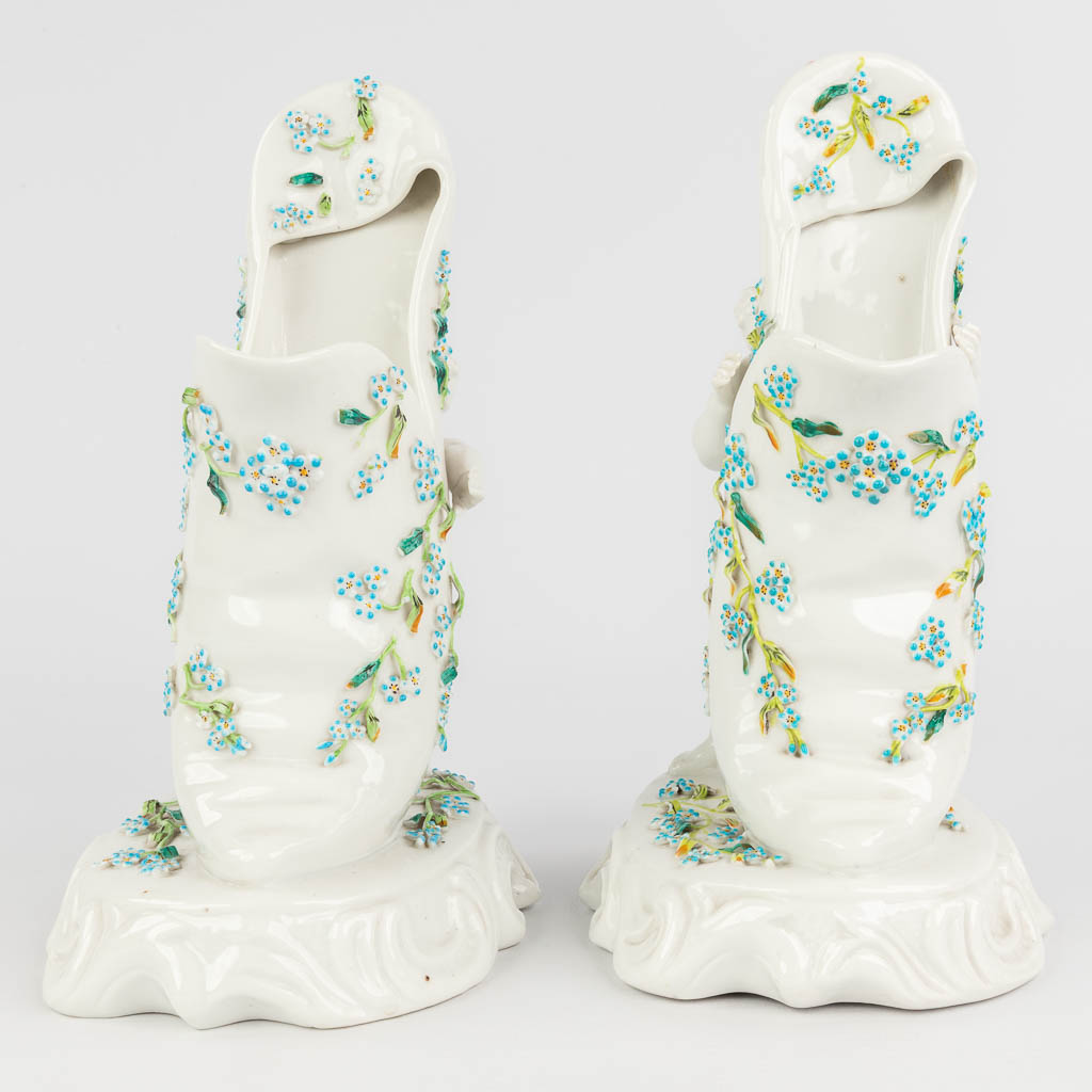 Sitzendorf, een paar bloemenvazen gemaakt uit porselein, in de vorm van 2 putti met een schoen. (L: 12,5 x W: 16 x H: 25 cm)