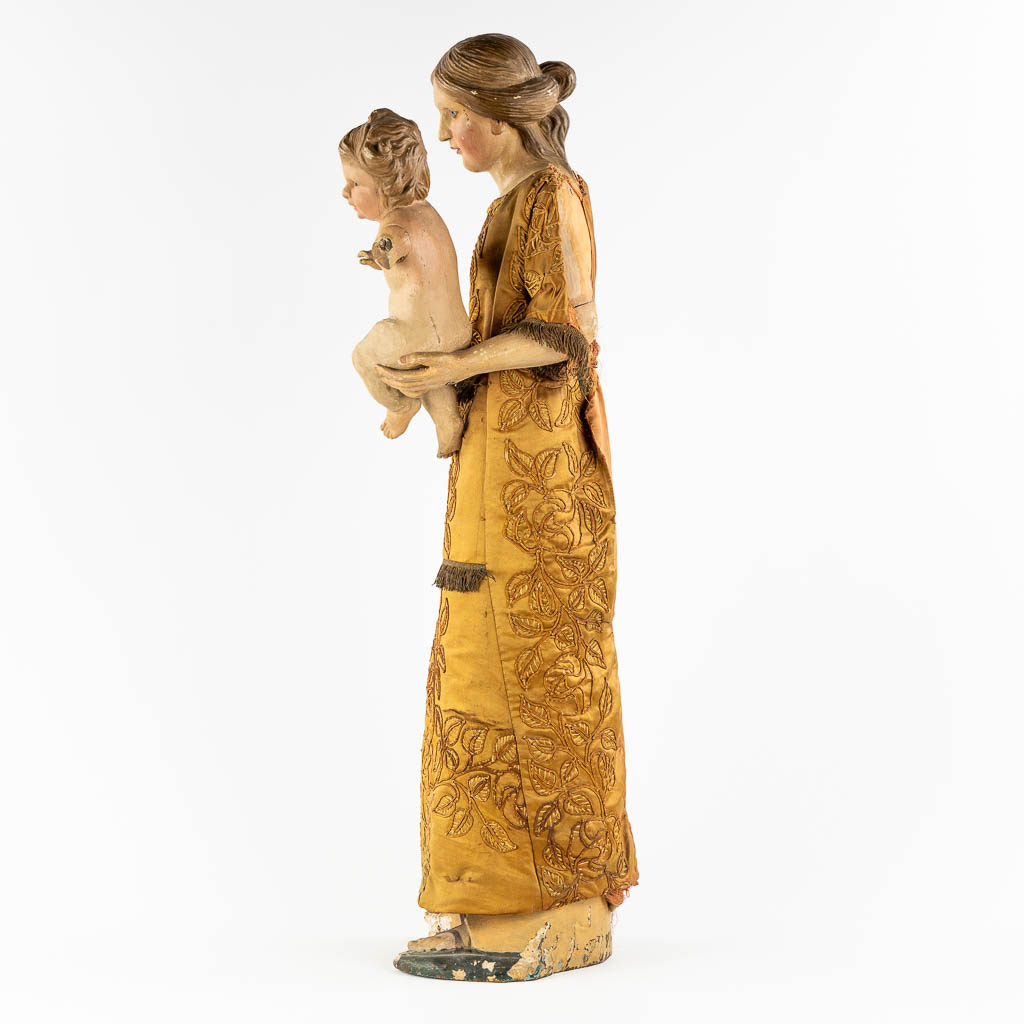 Een antiek houtgesculpteerd beeld van Moeder met kind, geborduurd kleed. 19de eeuw. (W:36 x H:97 cm)