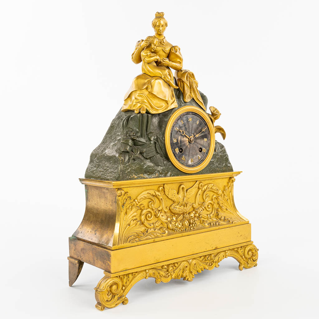 Een tafelklok gemaakt uit verguld en gepatineerd brons in empire stijl. Moeder met kind. (H:38cm)