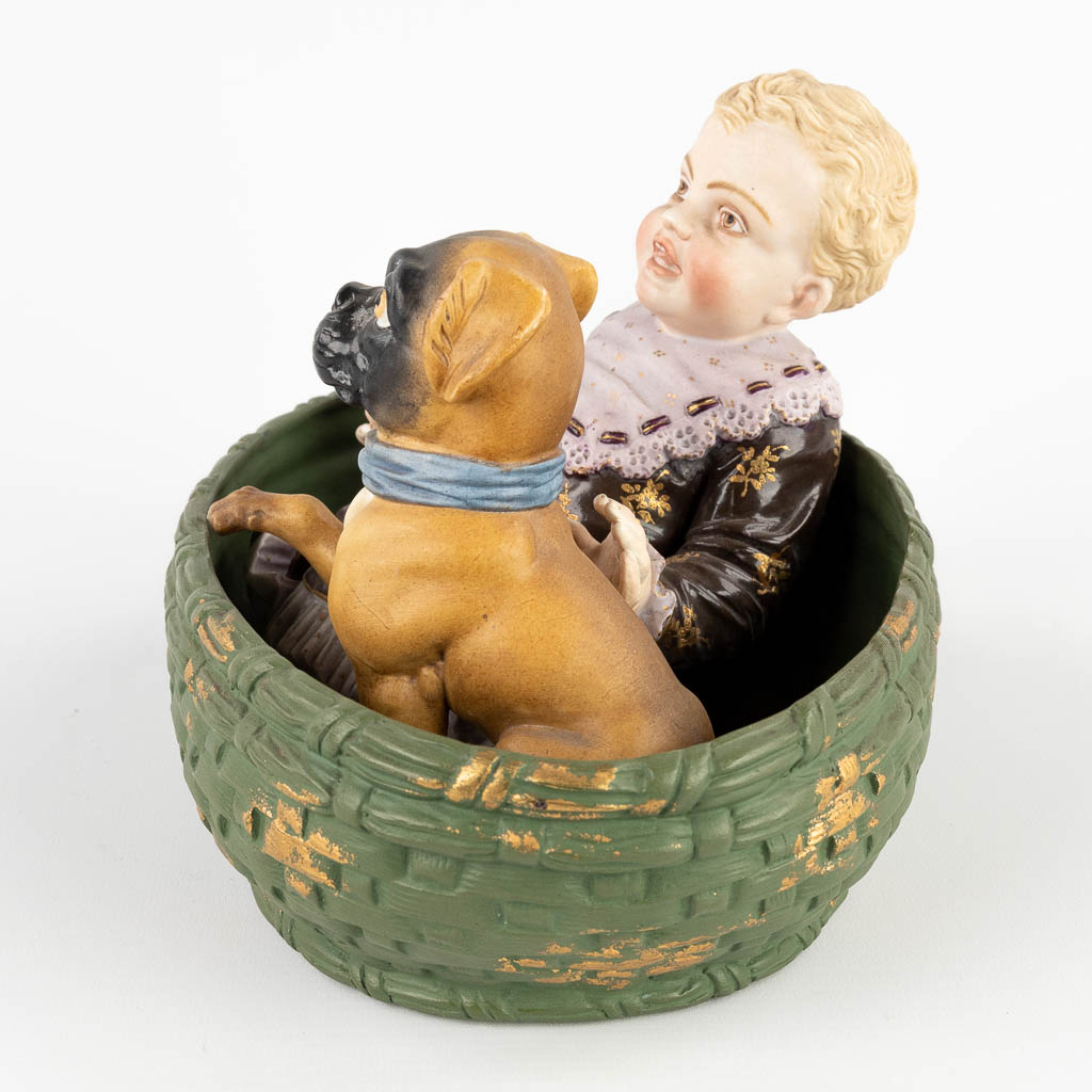 Child with a Pug, seated in a basket. Polychrome bisque porcelain. Circa 1900. (D:18 x W:24 x H:16 cm)