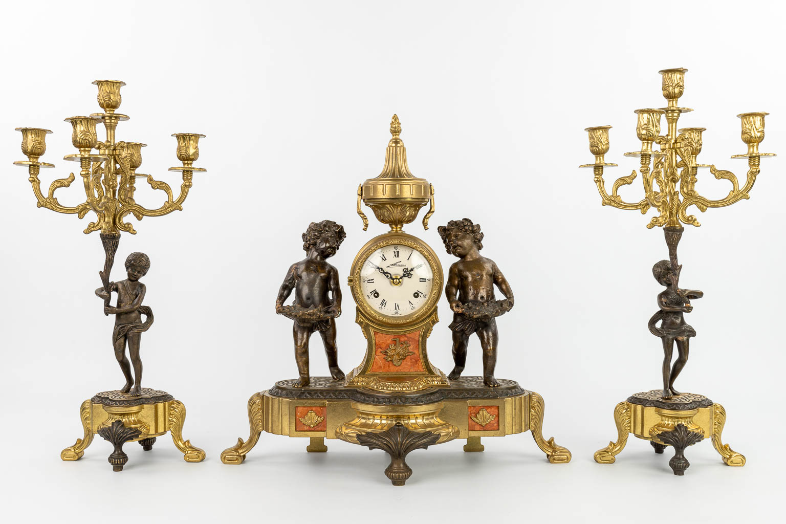 A three-piece mantle clock made of patinated and polished bronze, decorated with putti. (H:46cm)