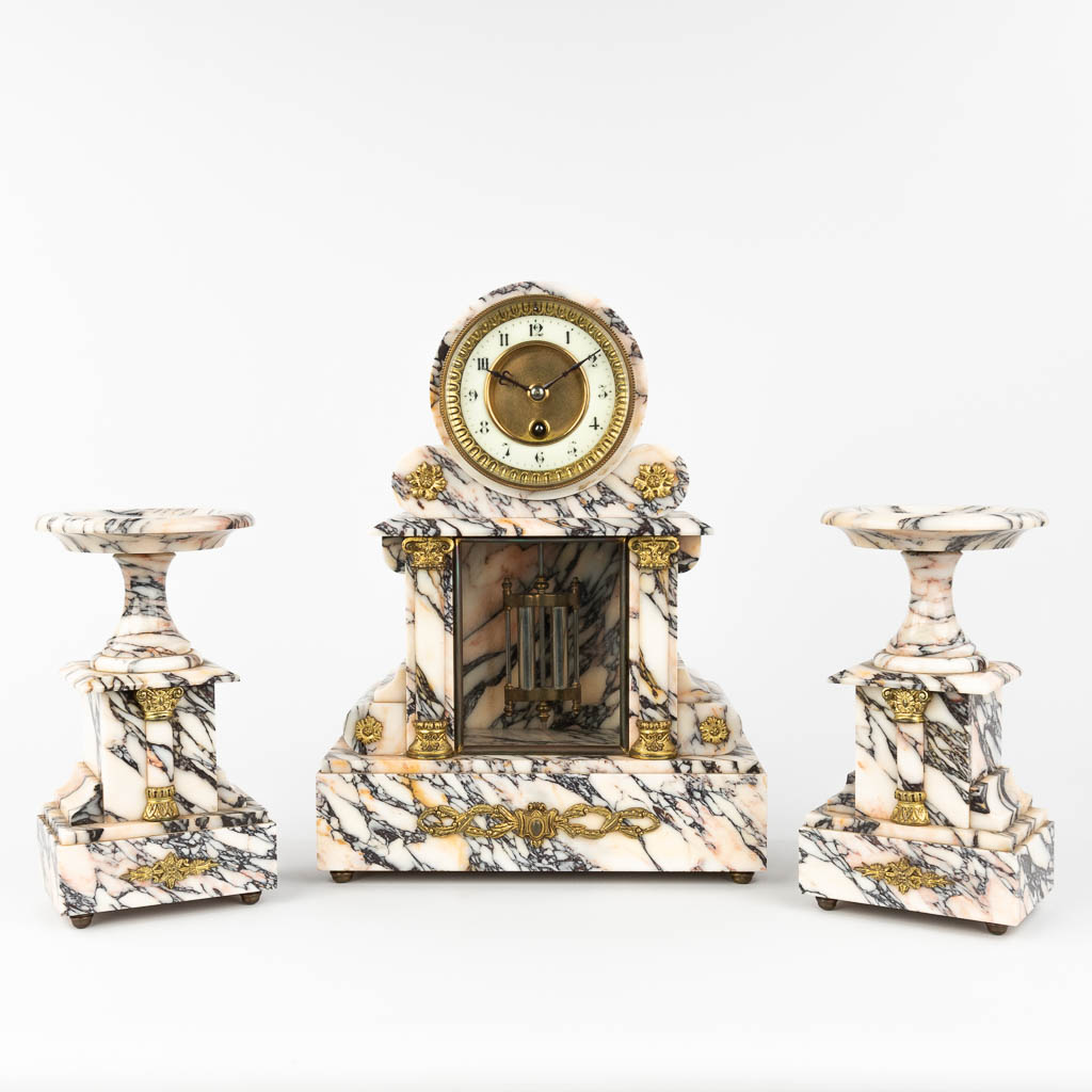 A three-piece garniture clock and side pieces, made of white and gray marble. Circa 1900. (L: 12 x W: 28 x H: 37,5 cm)