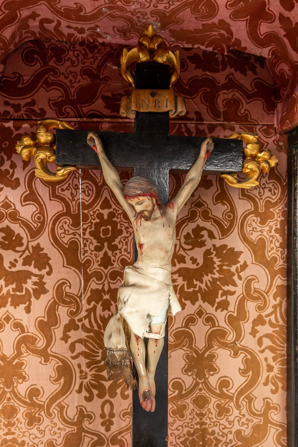 Een groot schrijn met een kruisbeeld, houtsculpturen en afgewerkt met stof. (D:30 x W:51 x H:97 cm)