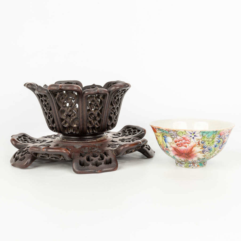 A Chinese porcelain bowl with a floral decor in a sculptured wood lotus flower stand. Marked Qianlong. (H:9,5cm)