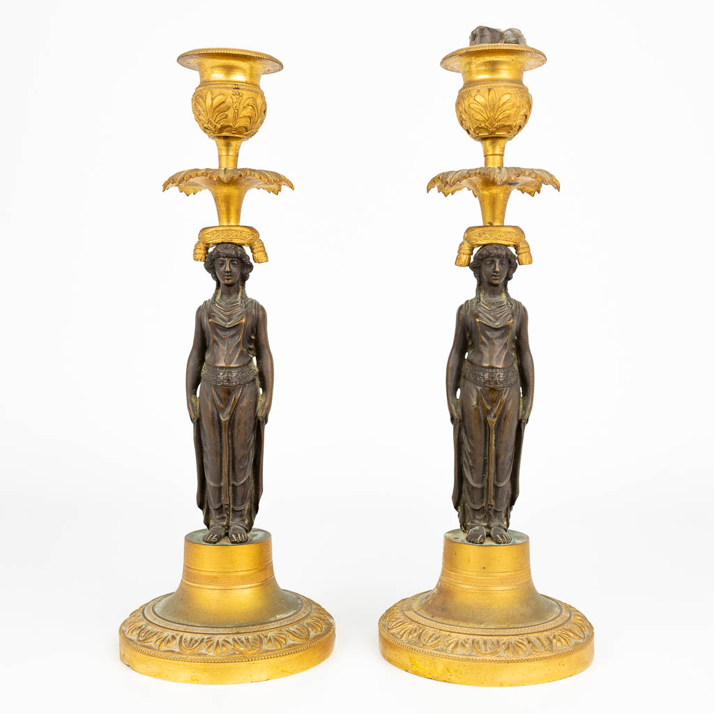 Een paar karyatide kandelaars, gemaakt uit verguld en gepatineerd brons in de empire periode, Eerste helft 19de eeuw. (H:27cm)