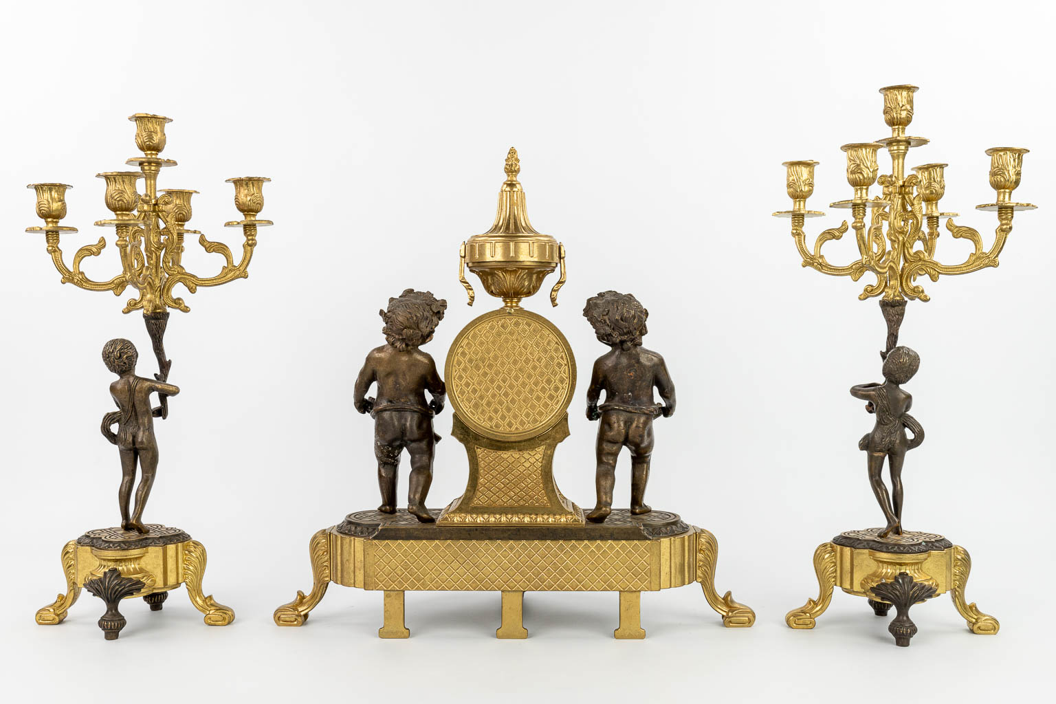 Een driedelige schouwgarnituur gemaakt uit verguld en gepolijst brons, versierd met putti. (H:46cm)