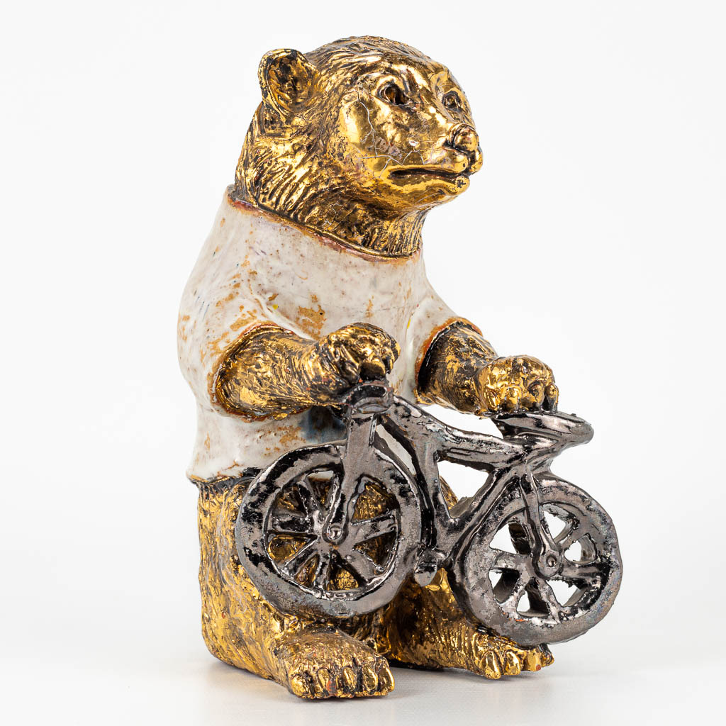 Elisabeth VANDEWEGHE (XX-XXI)A ceramic figurine of a bear with bicycle, with gold and white glaze. Perignem. 