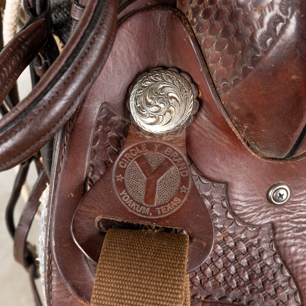 Circle Y Brand Yoakum Texas, Een zadel gemaakt uit leder, beenbeschermers en een lasso. (D:60 x W:70 x H:100 cm)