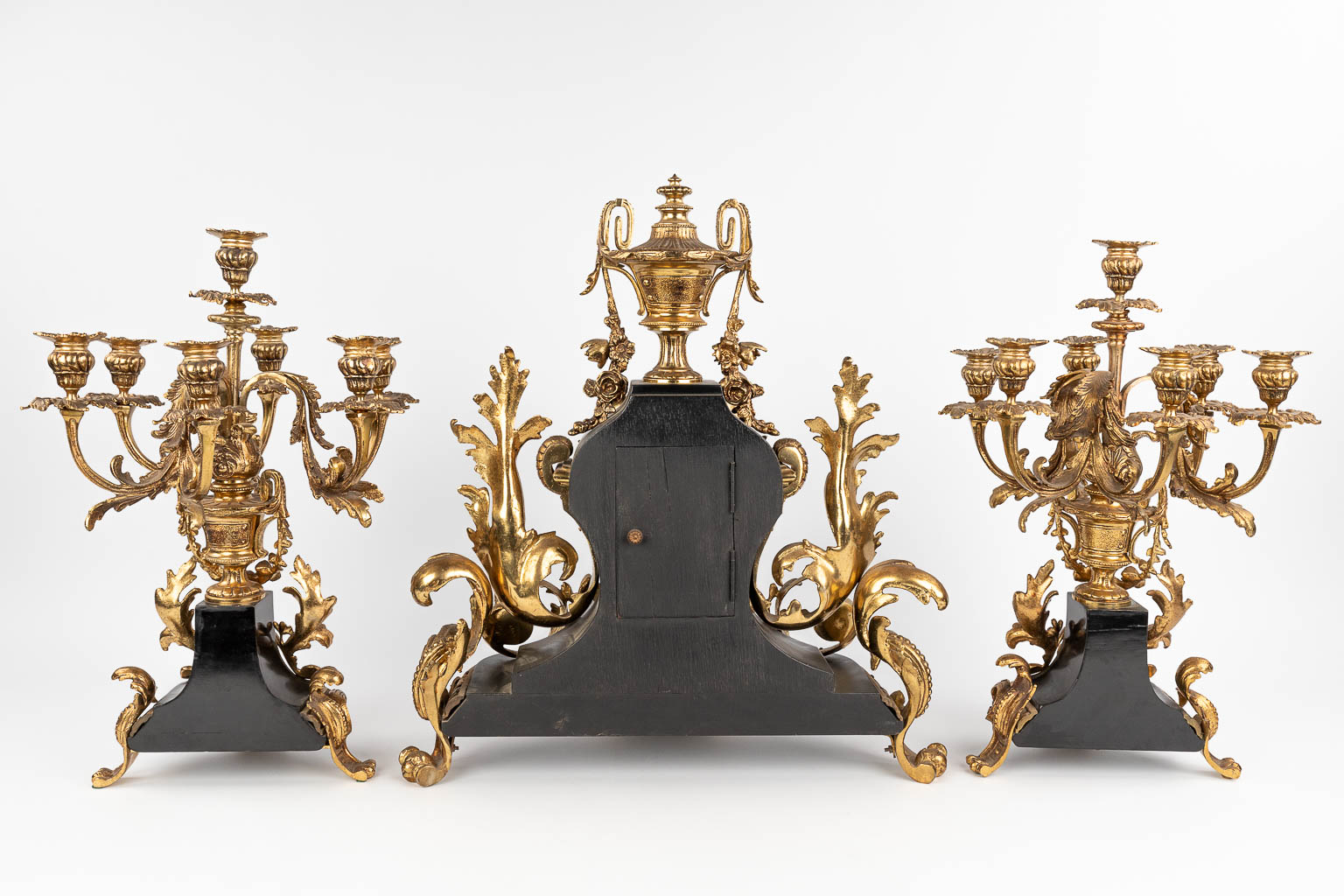Een driedelige schouwgarnituur bestaande uit een klok met kandelaars, Lodewijk XV stijl. Circa 1970. (L: 25 x W: 51 x H: 55 cm)