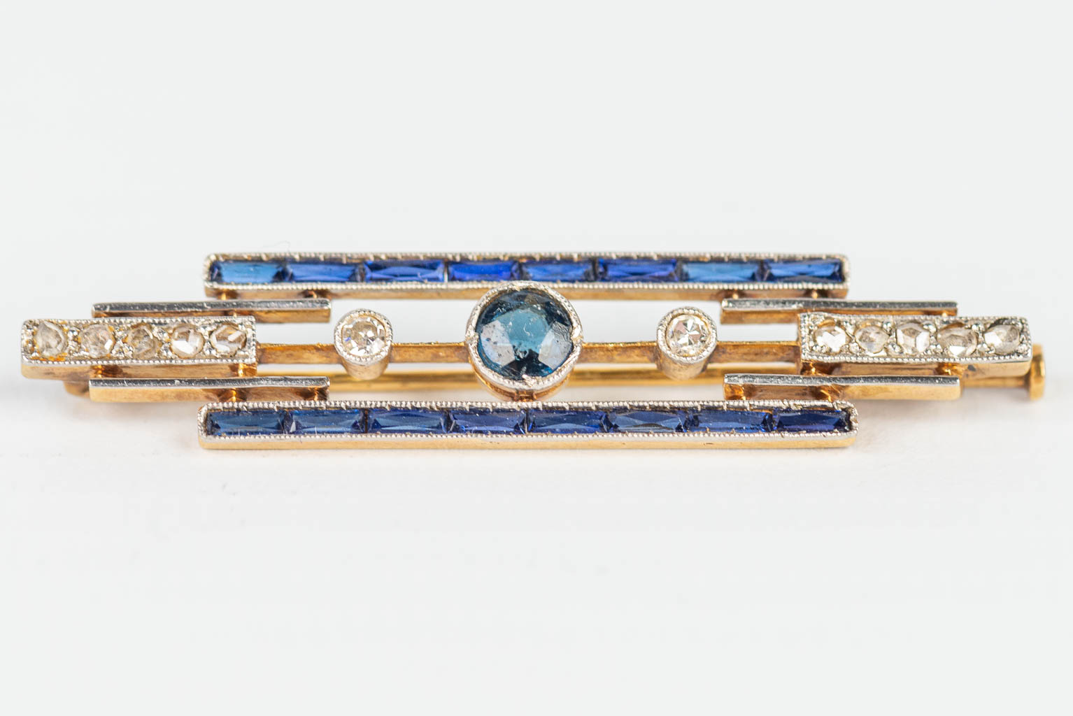A small brooch made of yellow and white gold in art deco style, with blue sapphires. 
