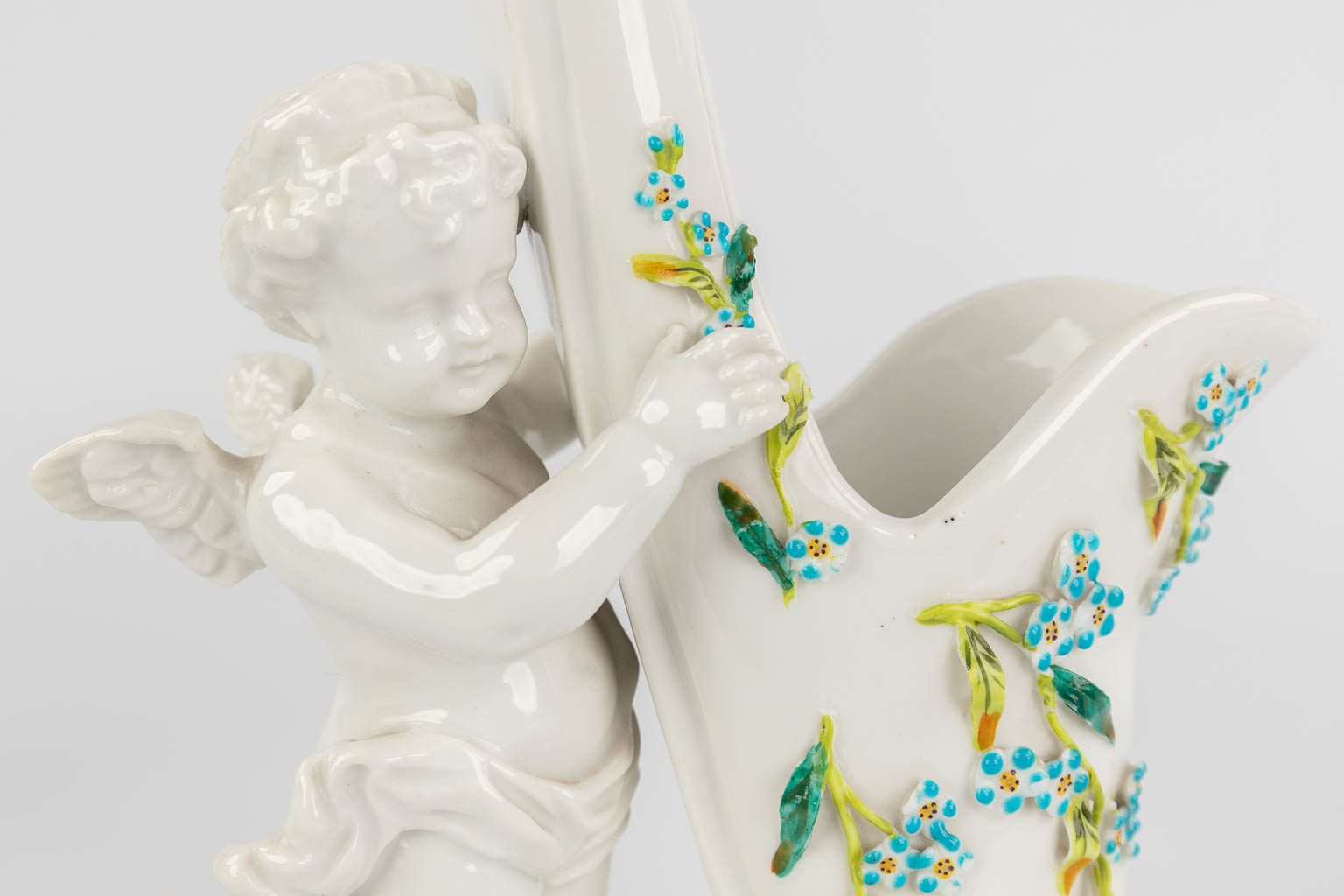 Sitzendorf, A pair of porcelain flower vases in the shape of 2 putti holding a shoe. (L: 12,5 x W: 16 x H: 25 cm)