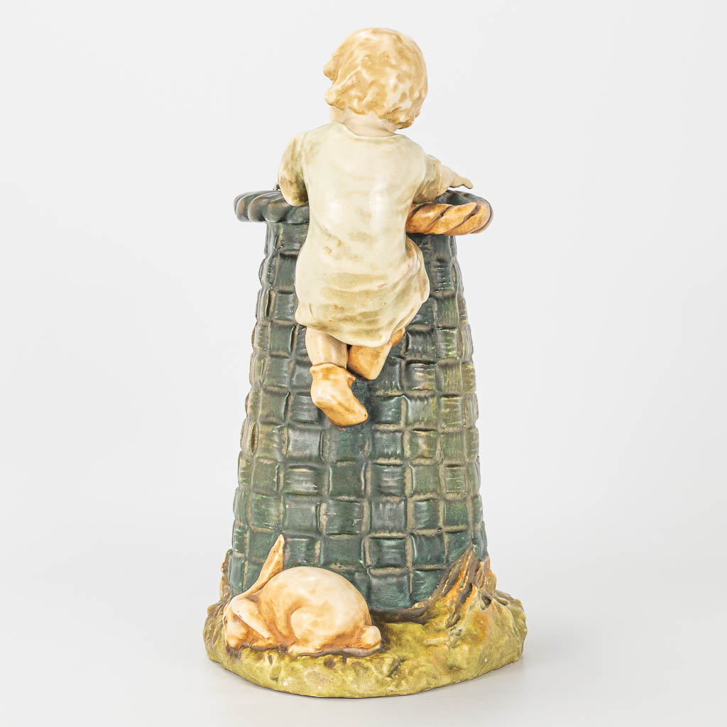 A ceramic statue of a child and rabbit by a large basket, marked Amphora, Austria. 