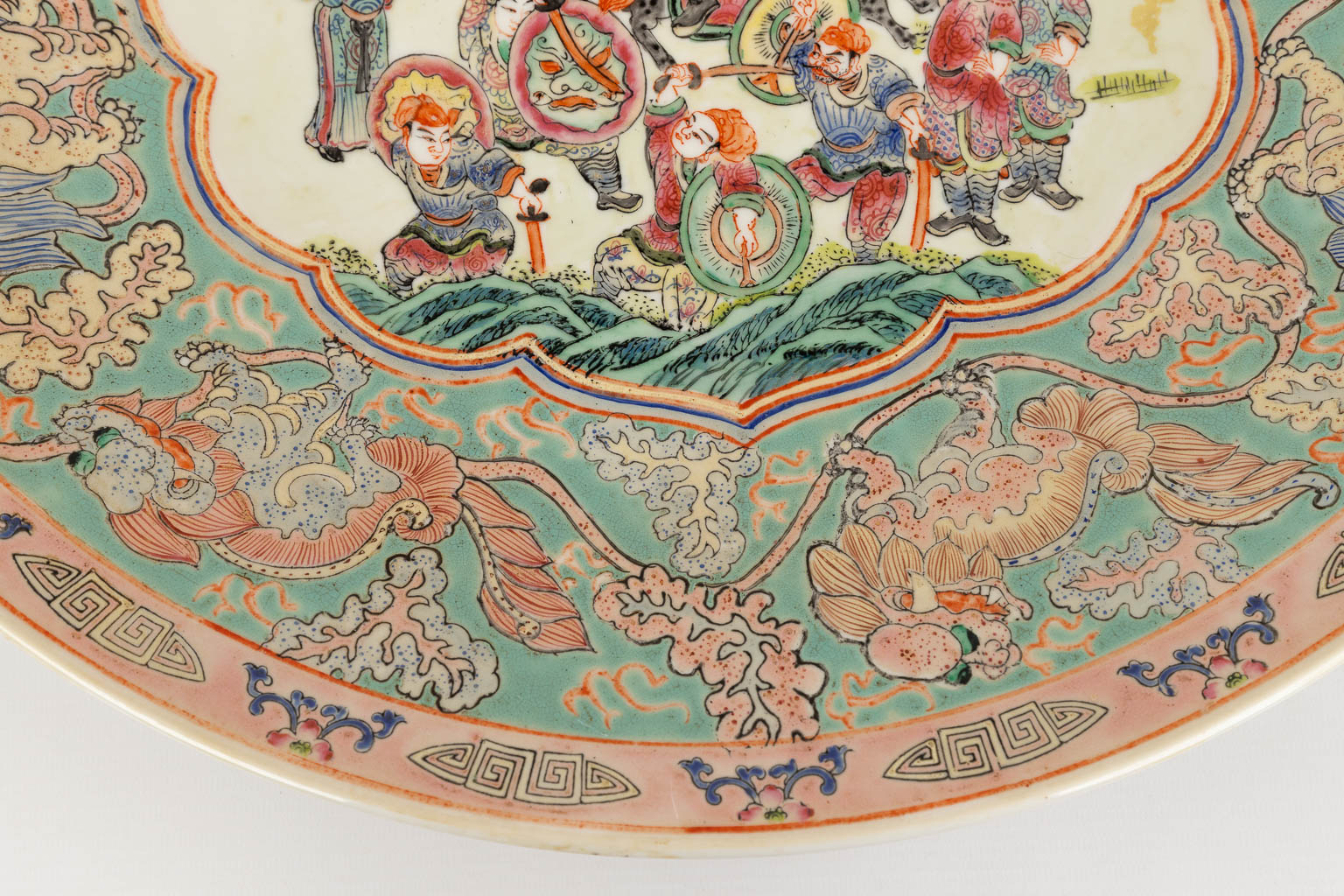 Een Chinees Famille Rose sierbord, decor van krijgers, perzikken en Foo Honden. 19de/20ste eeuw. (D:45,5 cm)