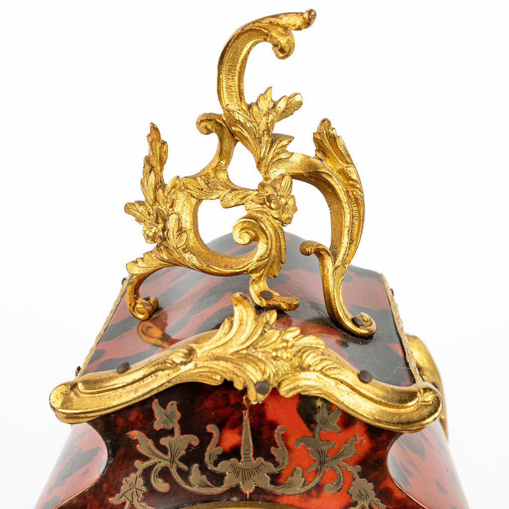 Een pendule afgewerkt met boulle inlegwerk en gemonteerd met brons in Lodewijk XV stijl. (H:33cm)