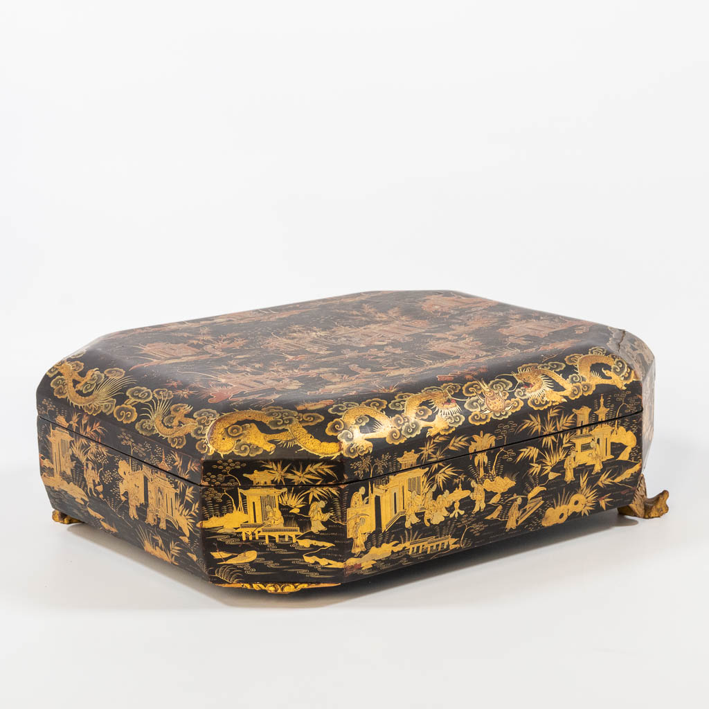 A Chinese lacquered storage box, with gold decor, on sculpured wood feet. 