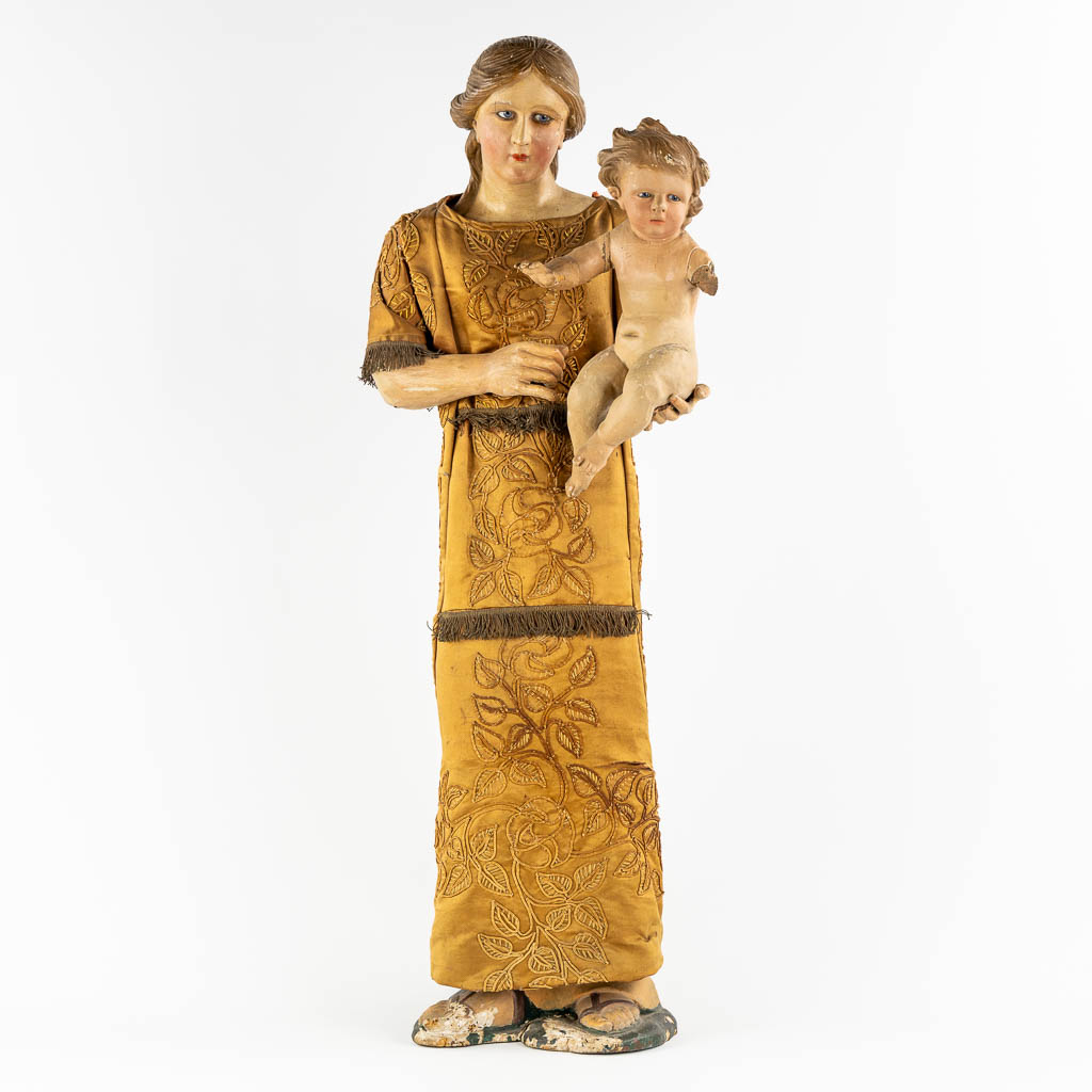 Een antiek houtgesculpteerd beeld van Moeder met kind, geborduurd kleed. 19de eeuw. (W:36 x H:97 cm)