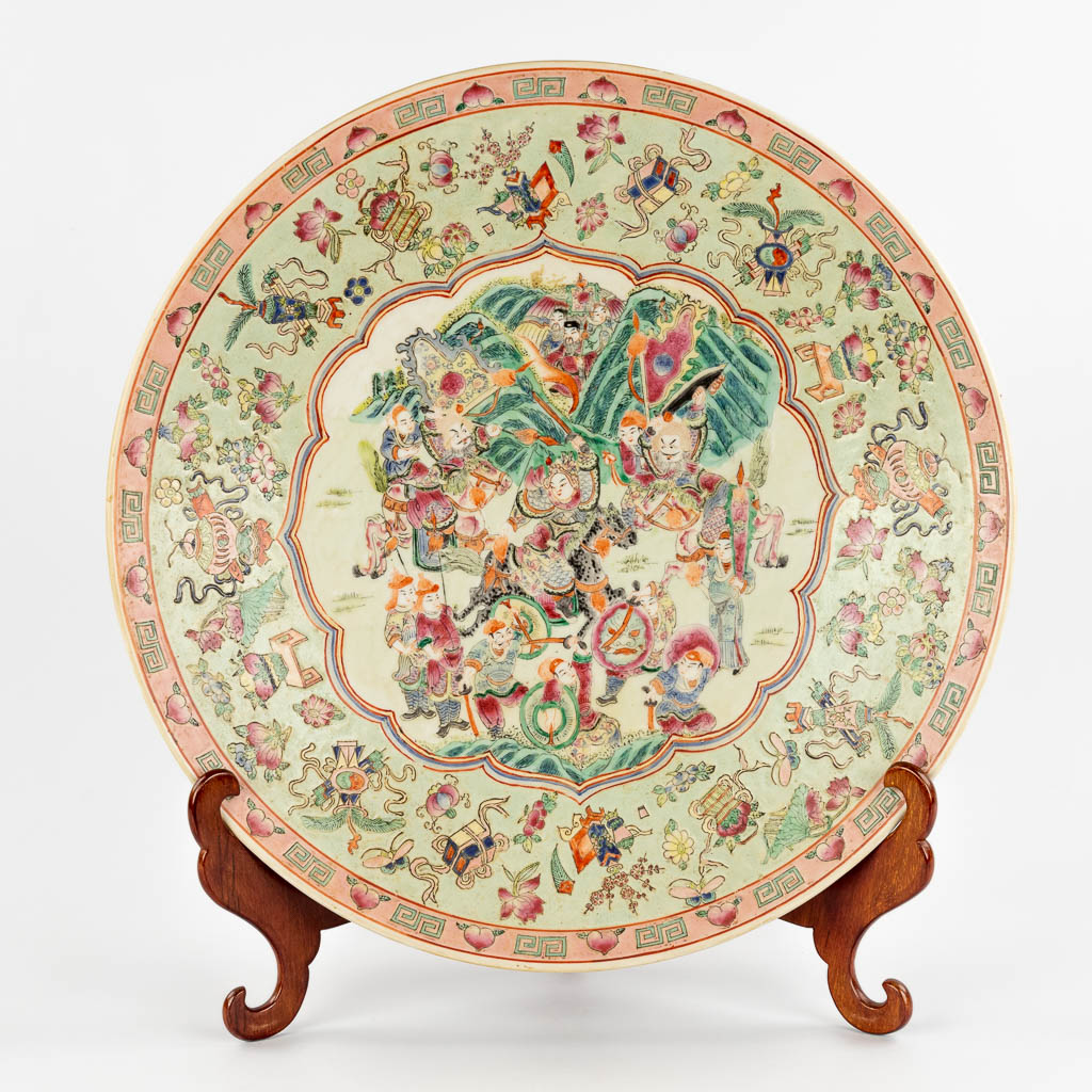 A Chinese Famille Rose plate, decorated with warriors, peaches and antiquities. 19th/20th C. (D:45,5 cm)