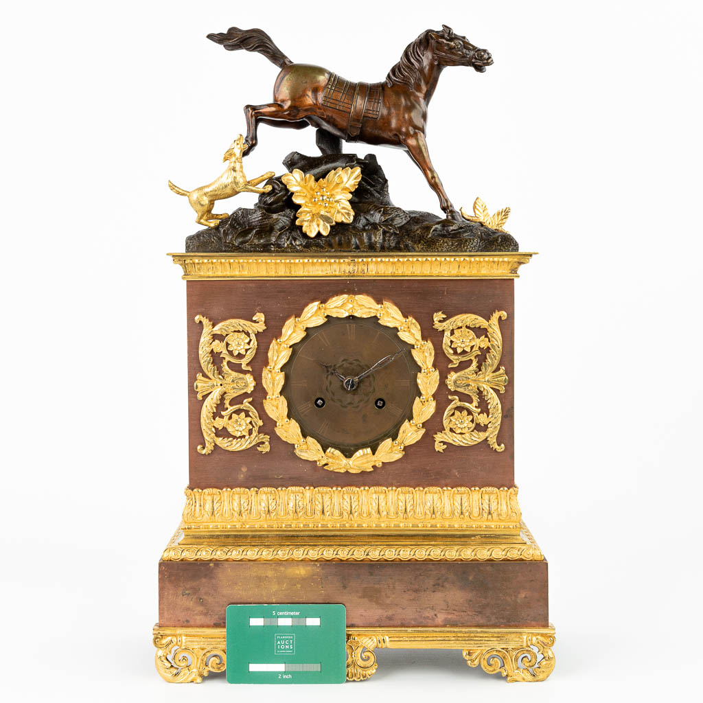 Een pendule afgewerkt met een paard en hond gemaakt uit brons in empire stijl. (H:48cm)