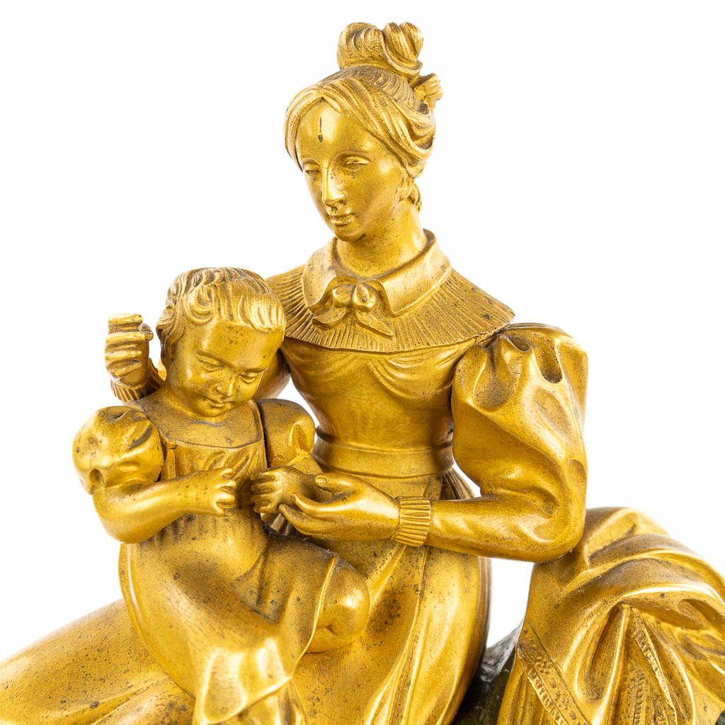 A table clock made of gilt and patinated bronze in empire style. Mother with child. (H:38cm)