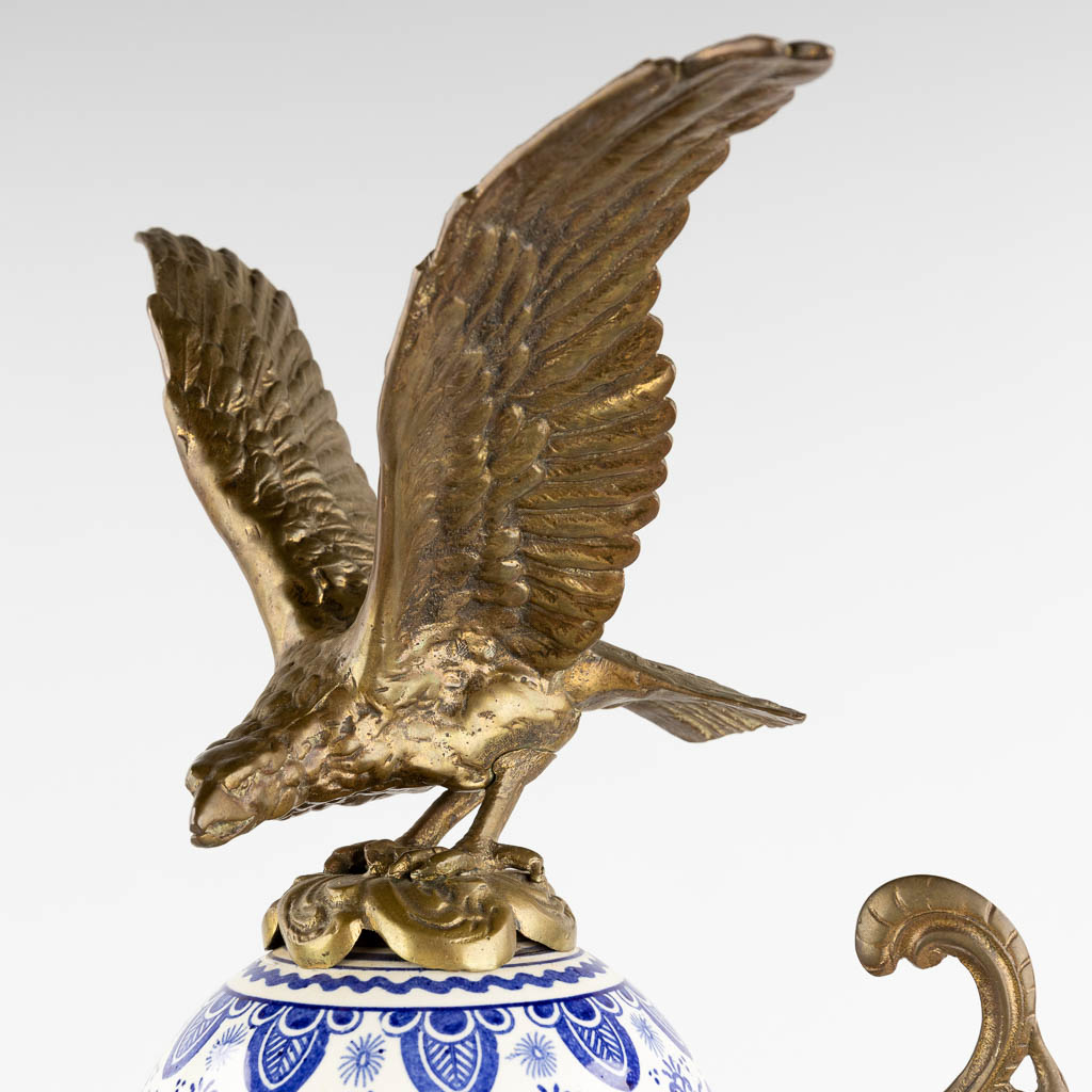 Een schouwklok, Delfts porselein gemonteerd met brons en afgewerkt met een arend. Circa 1900. (D:25 x W:44 x H:81 cm)