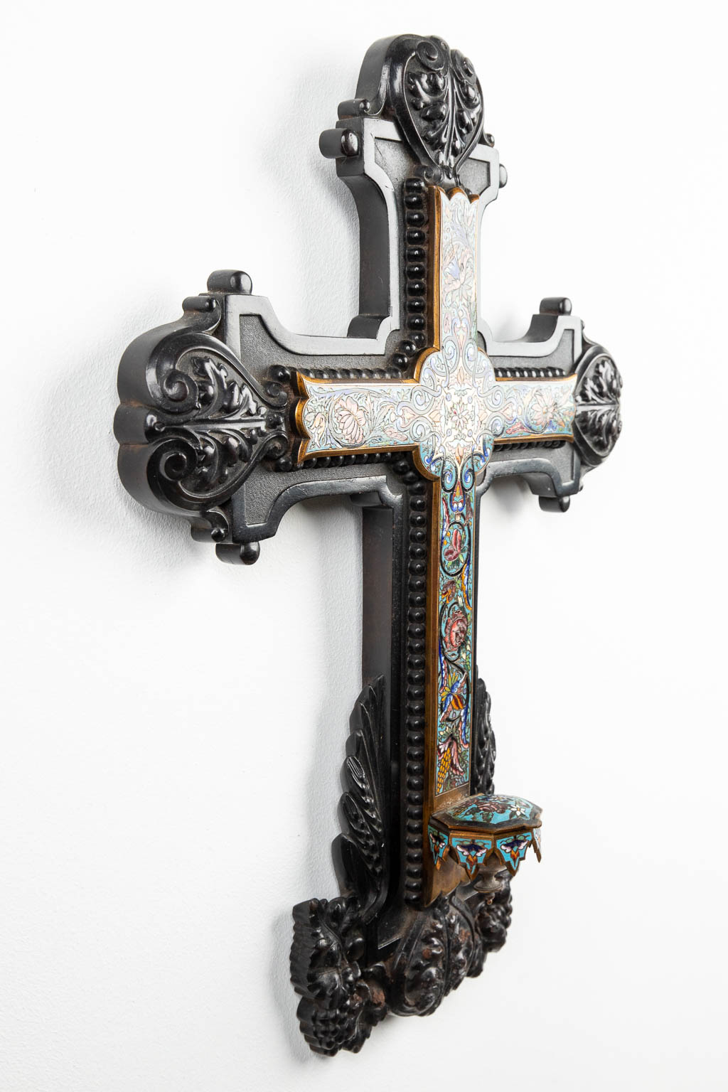 Een kruisbeeld afgewerkt met champleve inlegwerk en wijwatervat in gesculpteerd ebbenhouten kruis. (H:43cm)