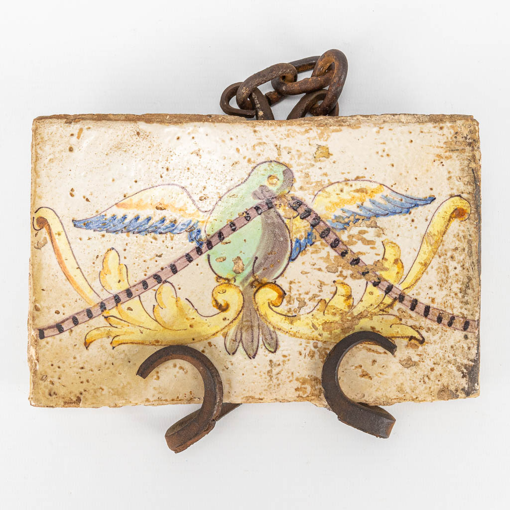 An antique tile with an image of a dove and mounted in a wrought iron frame