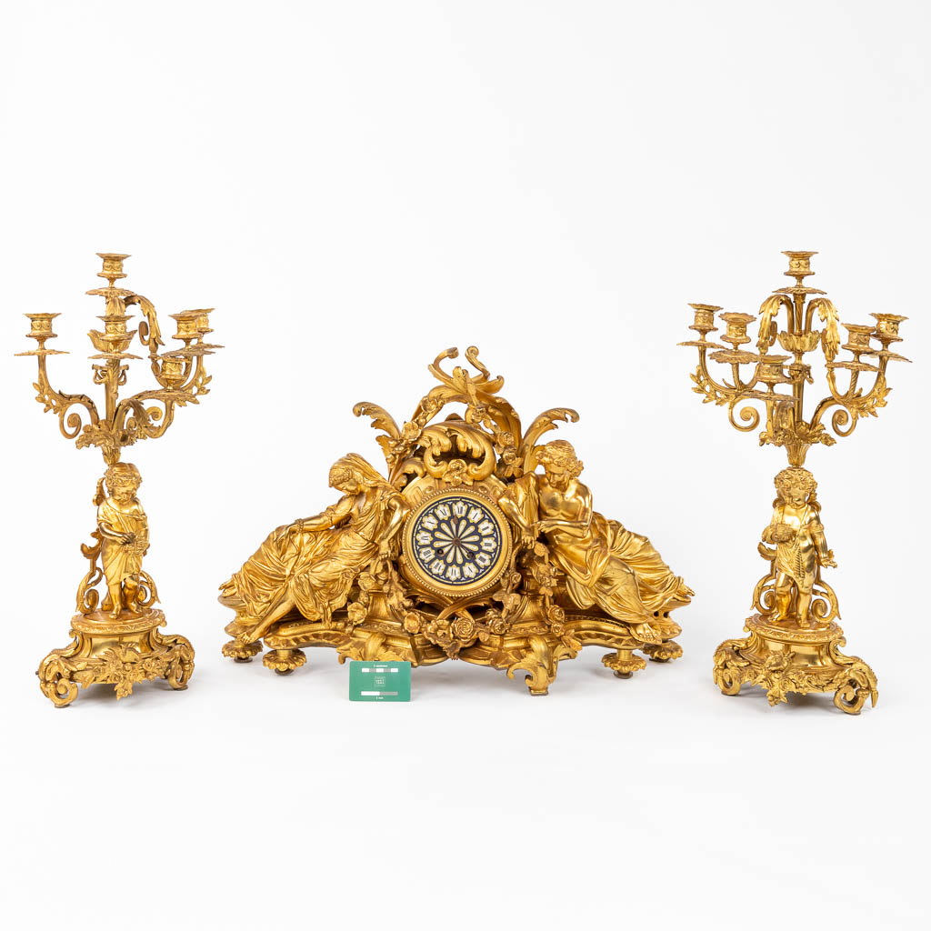 Een fijne, driedelige schouwgarnituur, verguld brons, Dame, heer en kandelaars met putti, 19de eeuw. (D:18 x W:72 x H:49 cm)