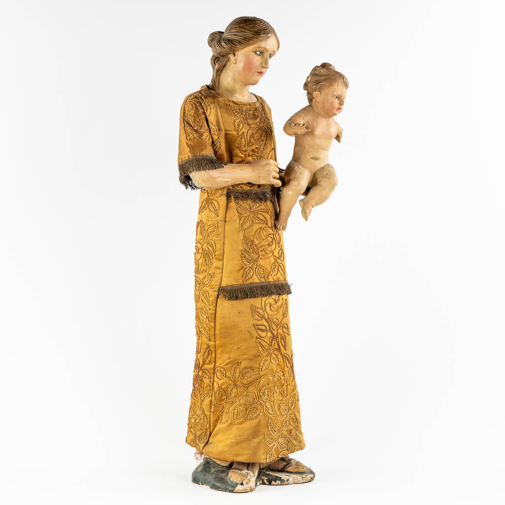 An antique sculptured figurine of a mother with child, wearing an embroidered robe. 19th C. (W:36 x H:97 cm)