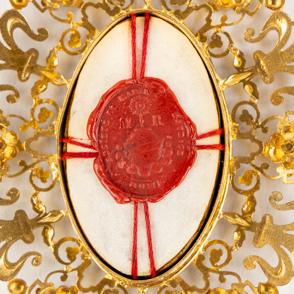 Een theca met relikwie voor de Kribbe van Jezus Christus, DNJC, in een messing relikwiehouder. (W:9,5 x H:13 cm)