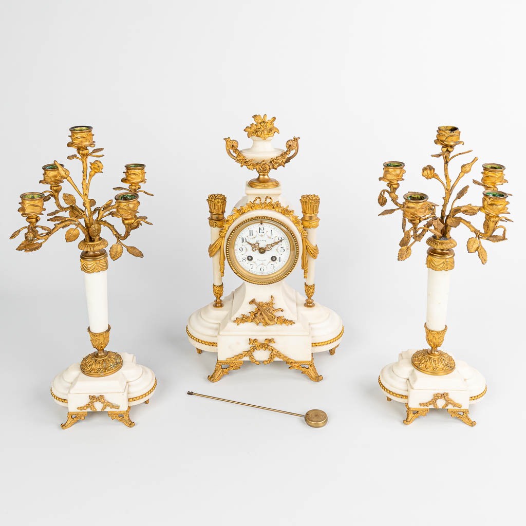 A three-piece mantle garniture with a clock and two candelabra made of white marble