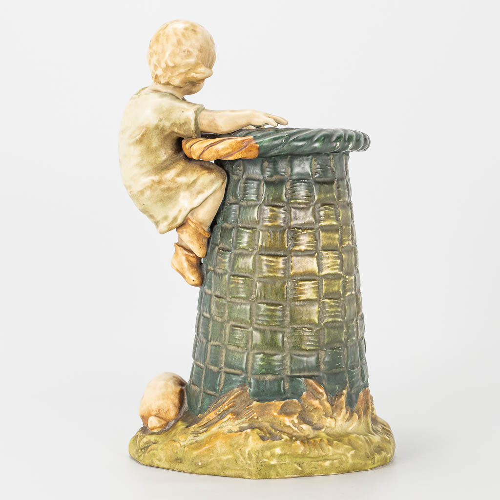 A ceramic statue of a child and rabbit by a large basket, marked Amphora, Austria. 