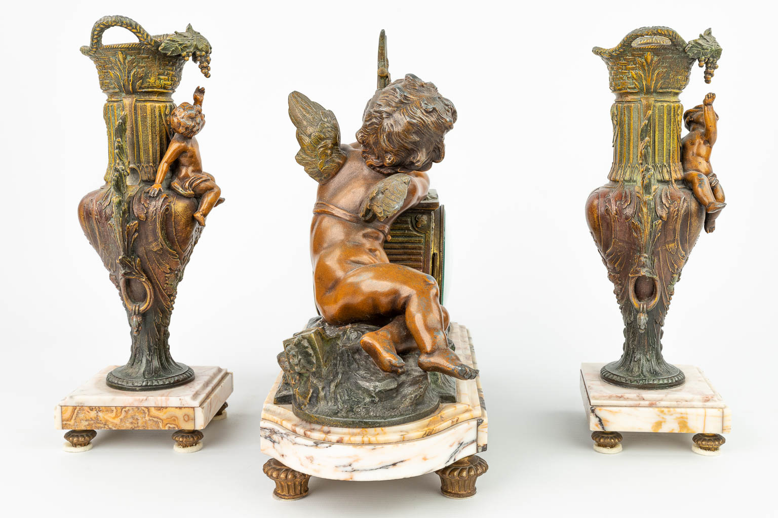A three-piece mantle clock made of spelter and decorated with putti. (H:33cm)