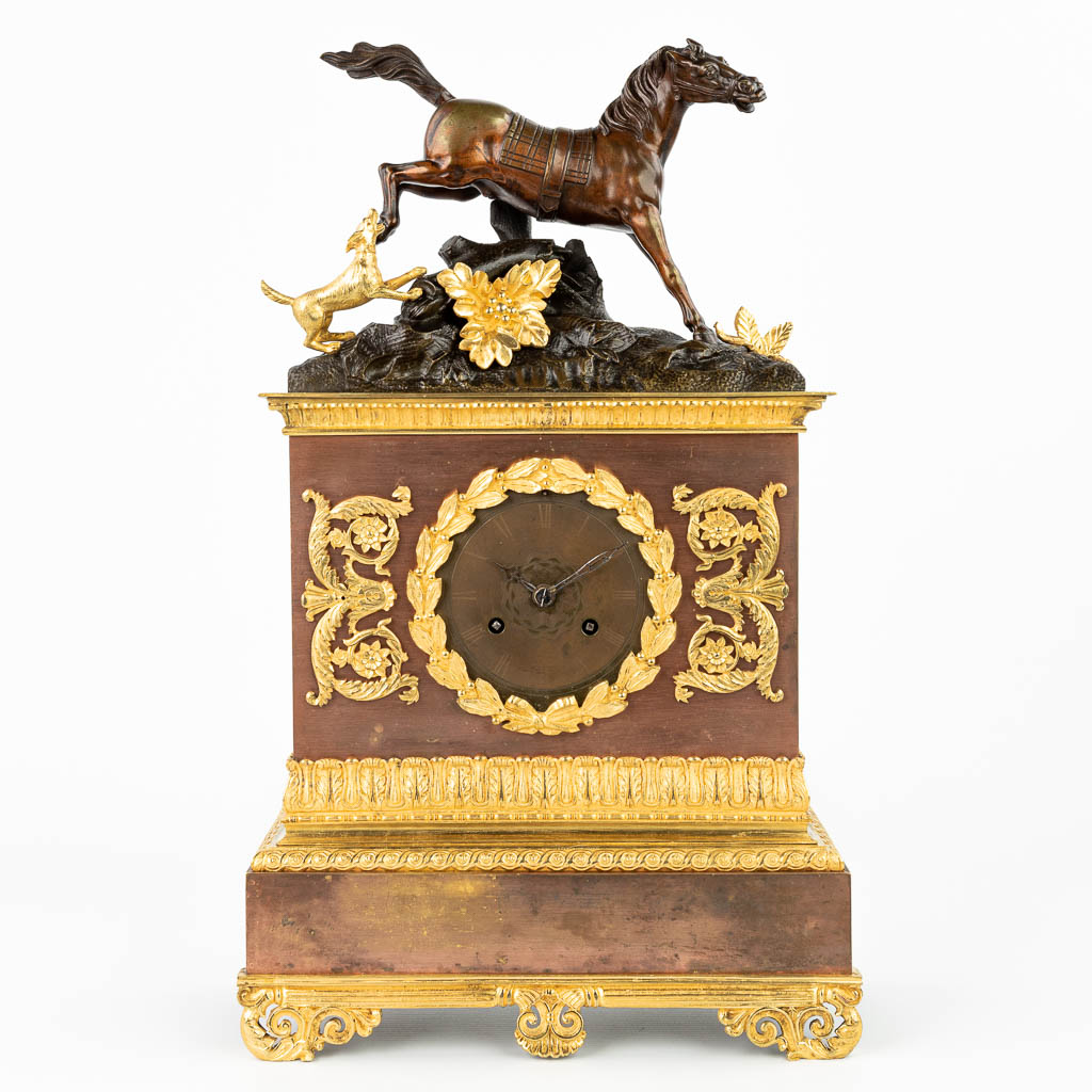 Een pendule afgewerkt met een paard en hond gemaakt uit brons in empire stijl. (H:48cm)
