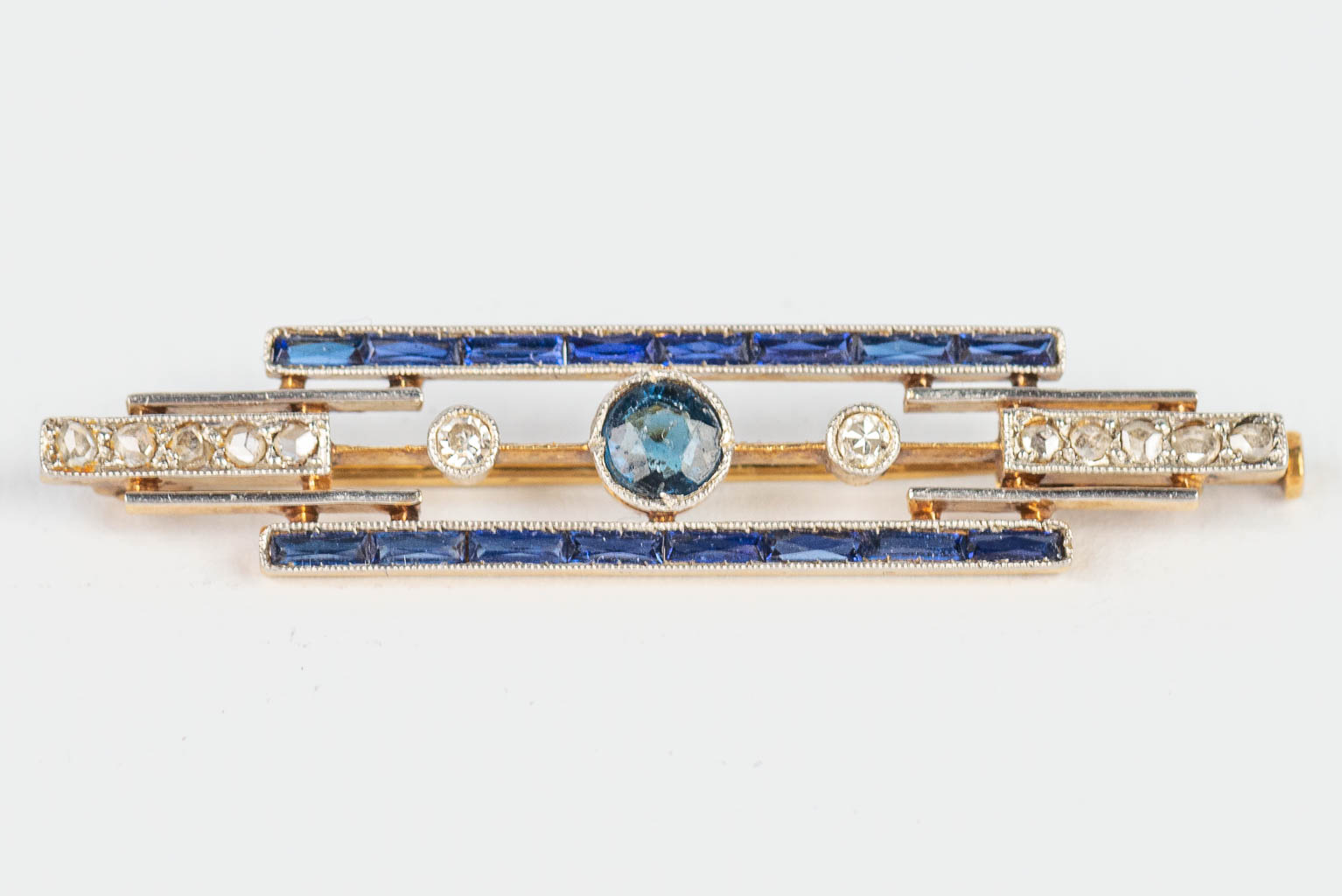 A small brooch made of yellow and white gold in art deco style, with blue sapphires. 