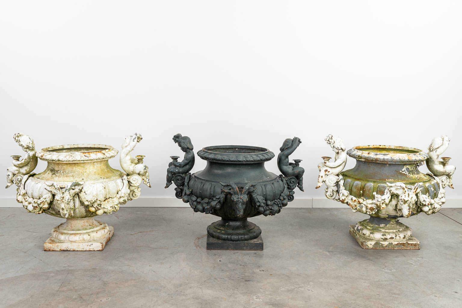 A set of 3 large garden vases made of cast iron, decorated with putti and ram