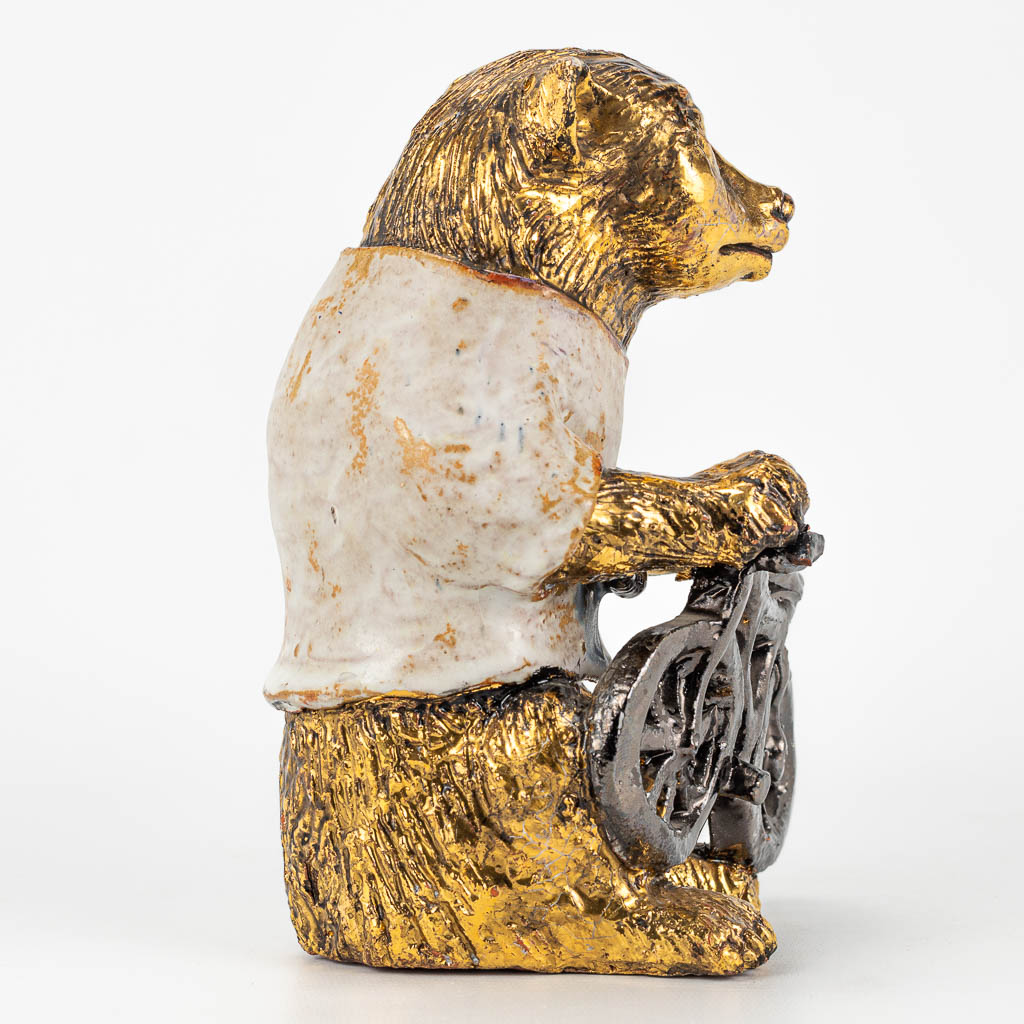 Elisabeth VANDEWEGHE (XX-XXI)A ceramic figurine of a bear with bicycle, with gold and white glaze. Perignem. 
