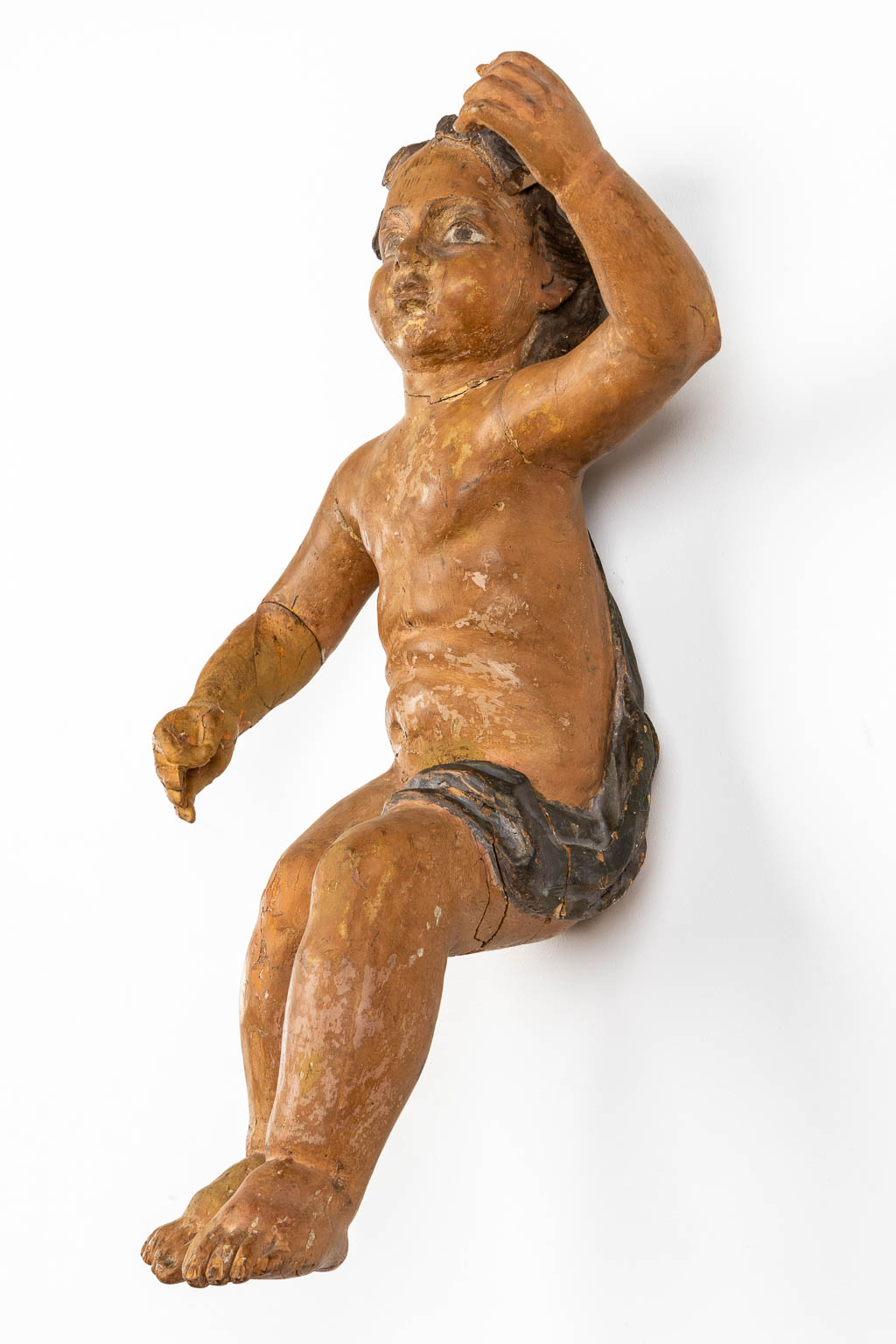 Een antieke figuur van een putto, gesculpteerd en gepatineerd hout. 18de eeuw. (L:35 x W:34 x H:67 cm)