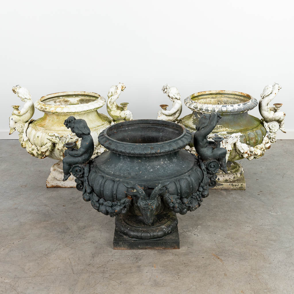 A set of 3 large garden vases made of cast iron, decorated with putti and ram's heads. (H:57cm)